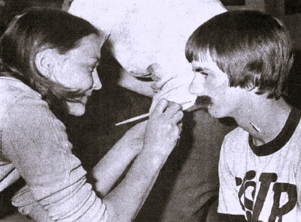 A makeup artist applies a fake mustache to a man.