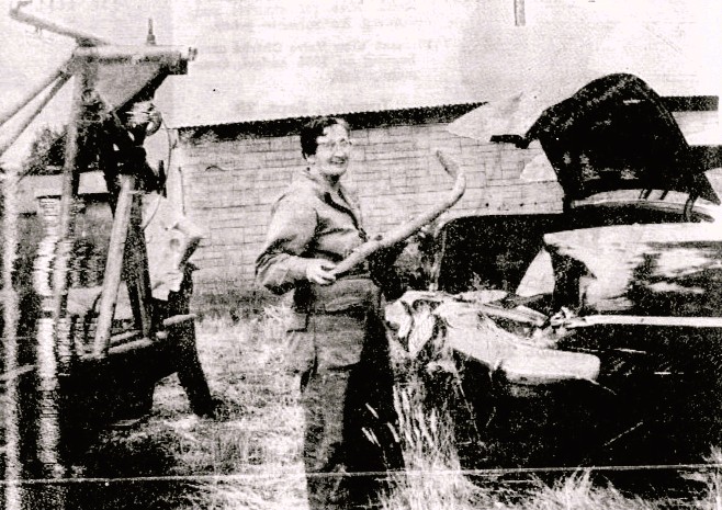 A woman holds a car part in a junk yard.