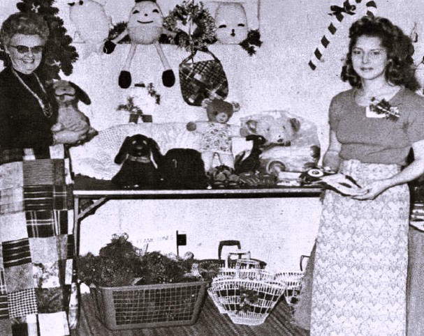 Two women stand next to a table filled with toys.