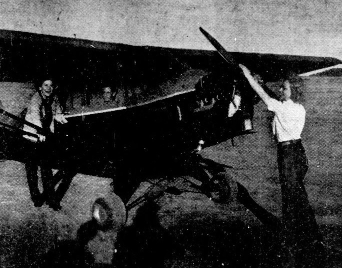 A woman starts the propeller of a small plane while another stands by the wing.