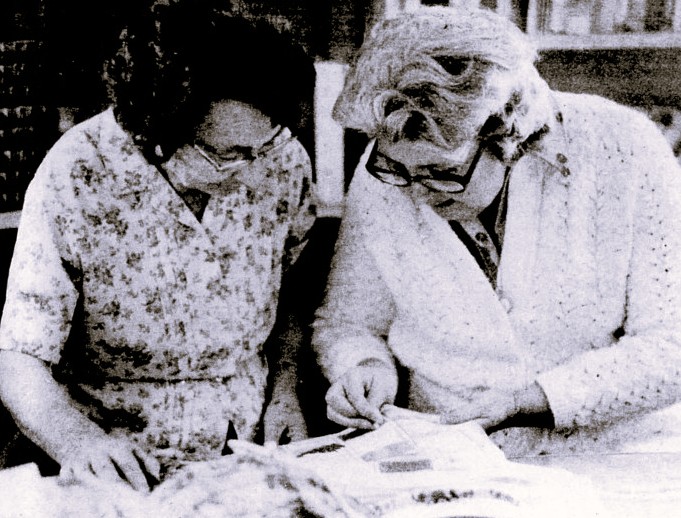 One woman shows her sewing project to another woman.