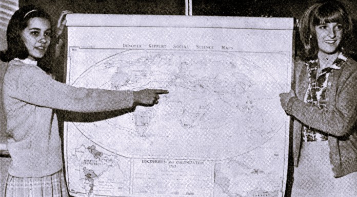 Two high school girls hold up a large map of the globe.