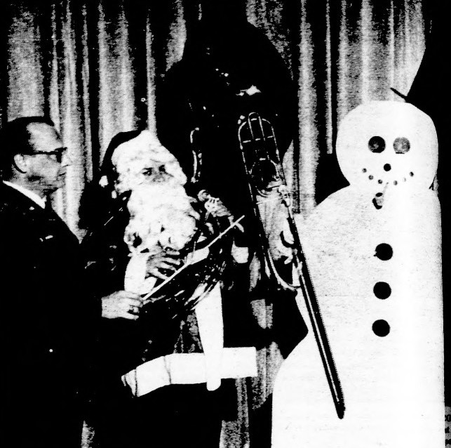 A conductor holds a baton while Santa plays the tuba and a snowman plays the trombone.