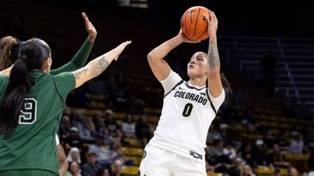 A University of Colorado Boulder basketball player shoots over the outstretched arms of two players on the opposing team.