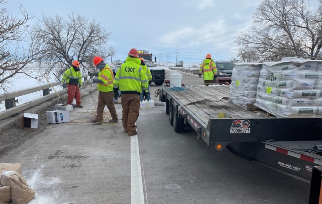 Four CDOT employees in high-visibility safety gear work examine a bridge that is under repair.