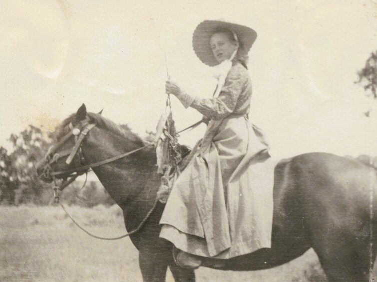 A girl wearing a dress and bonnet rides a horse.