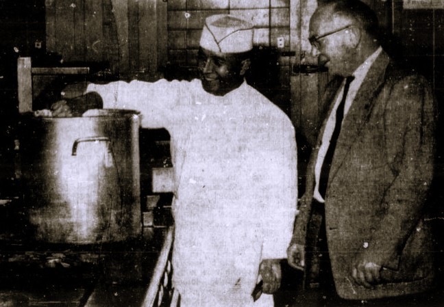 A chef stirs a large stockpot while another man looks on.