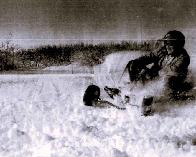 A person wearing a helmet drives a go-kart through the snow.