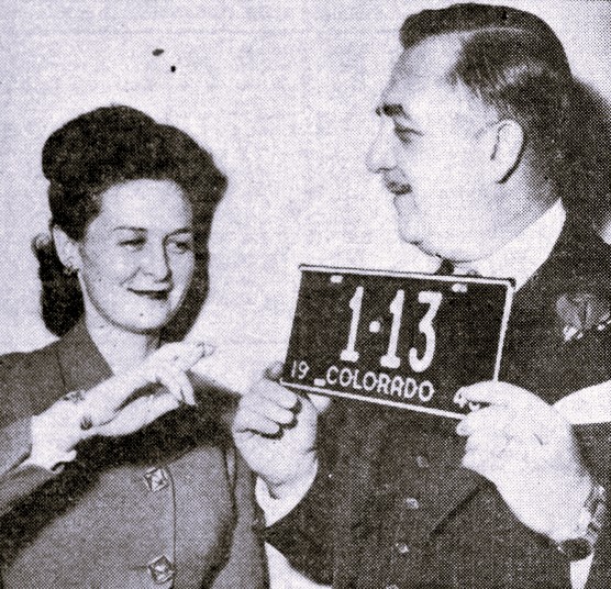 A woman crosses her fingers while a man holds up a license plate with the number 13.