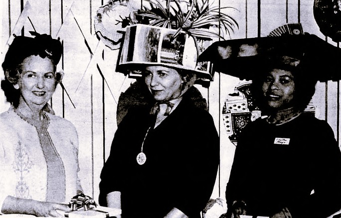 Three women model the abstract hats they created for a charity contest.