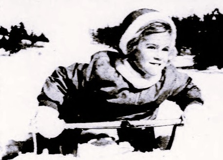 A child in winter clothes sleds downhill.
