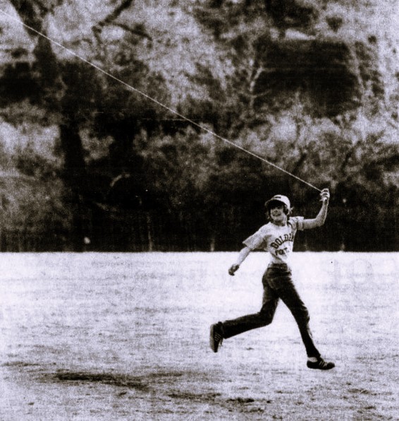 A boy wearing a baseball hat flies a kite.