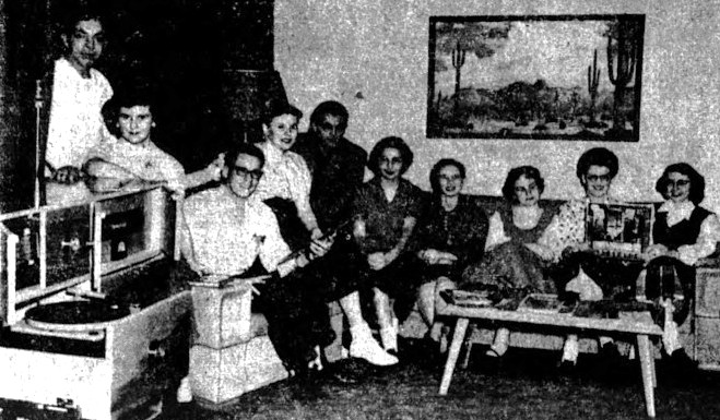 A college group of Hi-Fi enthusiasts sit on a couch next to a record player.