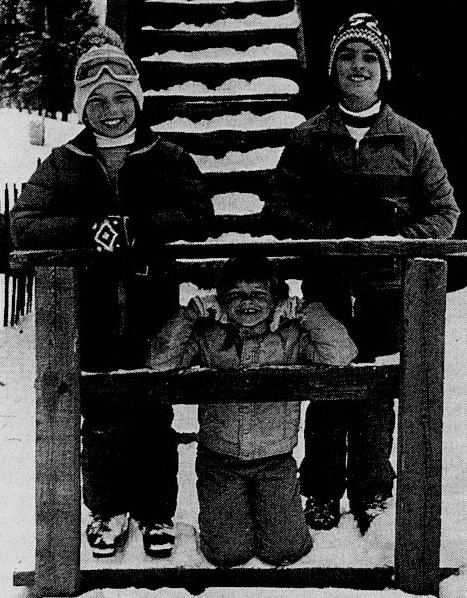 Three children in winter clothes pose on snowy steps