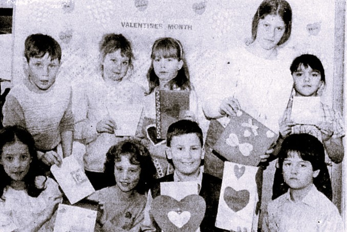 A classroom of children hold up their handmade Valentines.