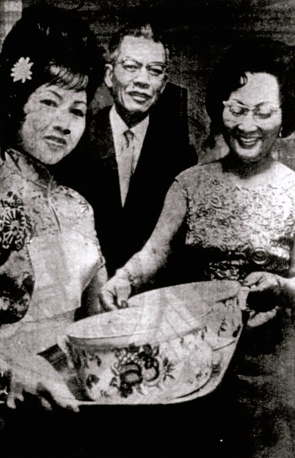 An Asian family wearing formal attire holds up decorative serving dishes.