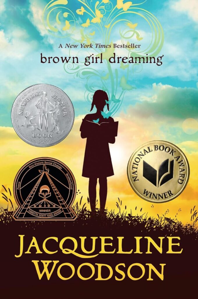 Cover Art for Brown Girl Dreaming. The silhouette of a girl with pig tails and dress standing in a brown field with the sky and sunset behind her.