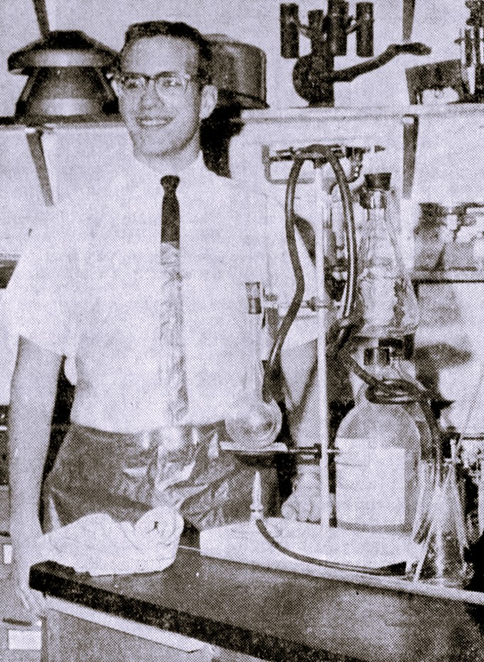 A high school boy stands next to chemistry equipment.