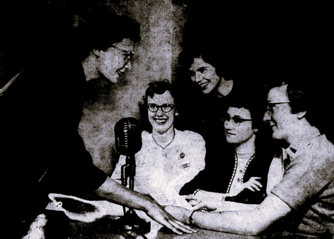 Five women gather around a microphone.