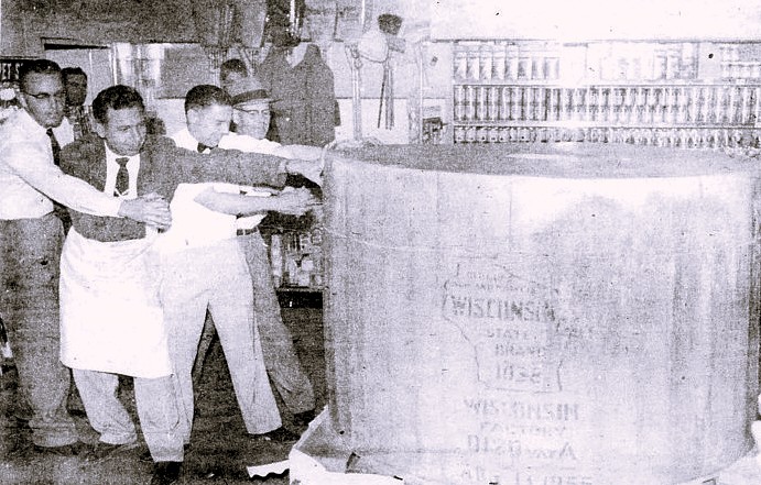 Four men cut a giant wheel of cheese.