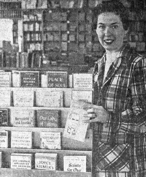 A woman in a plaid suit poses next to a book display in a library.