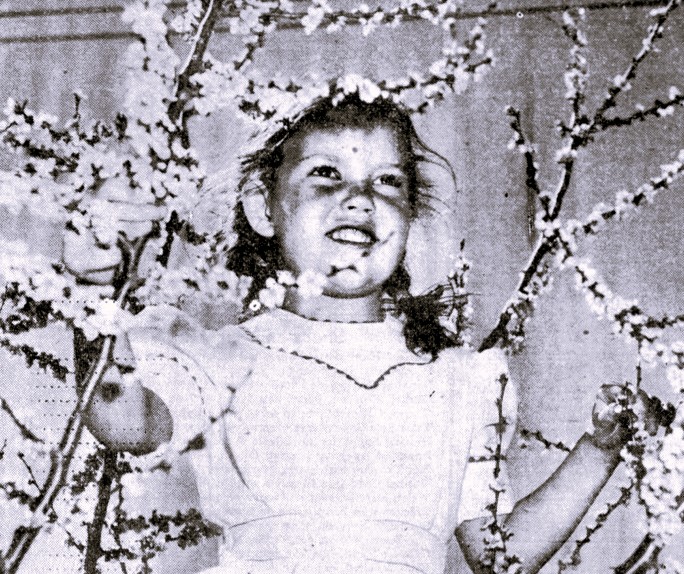 A girl stands amidst blossoming tree branches.