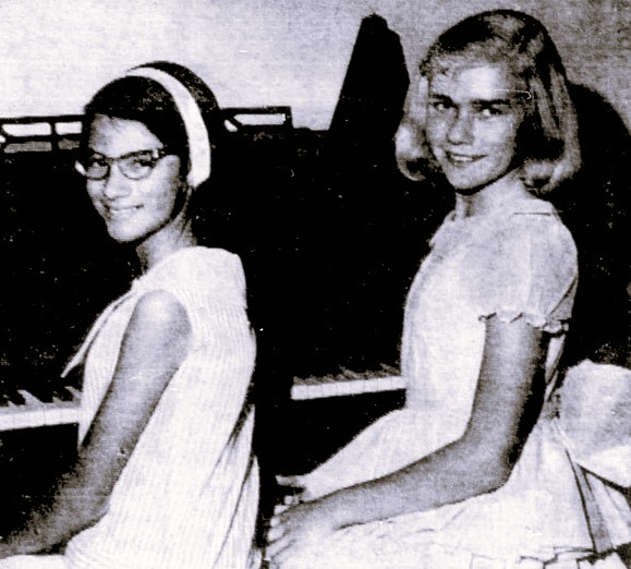 Two girls sit at a piano.