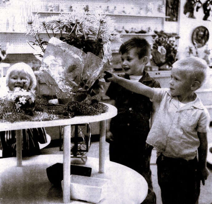 A young boy points at a bouquet of flowers while two other children stand nearby.