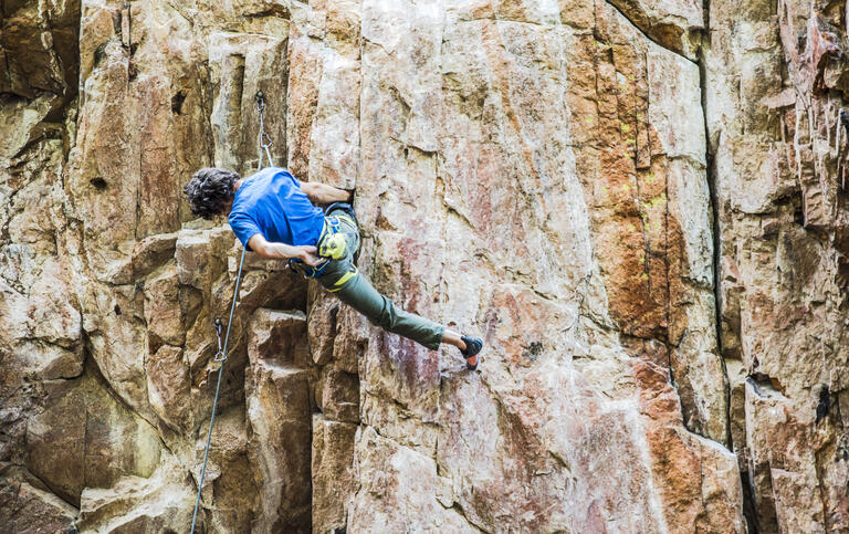 A rock climber hang off the side of a rock wall pauses to reach into a chalk bag.