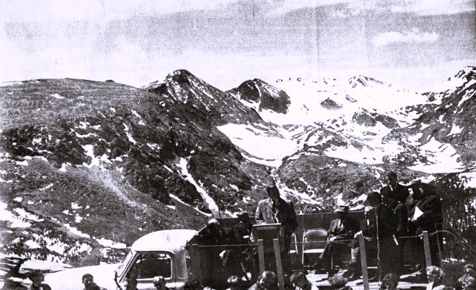 A man speaks at a podium set up on a truck bed, in front of a large mountain.