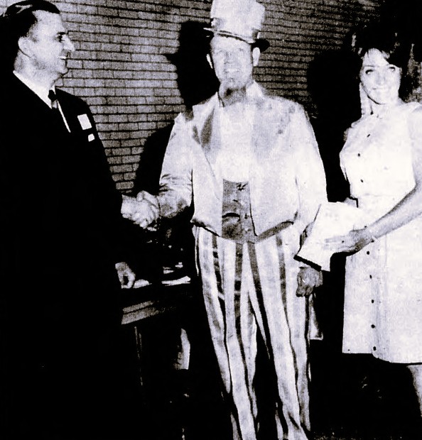 A man dressed like Uncle Sam shakes hand with another man while a woman looks on.