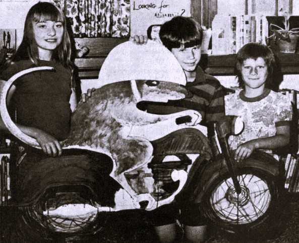 Three children stand next to a cardboard cutout of a mouse riding a motorcycle.