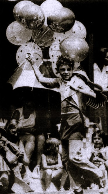 A boy carries balloons in a parade.