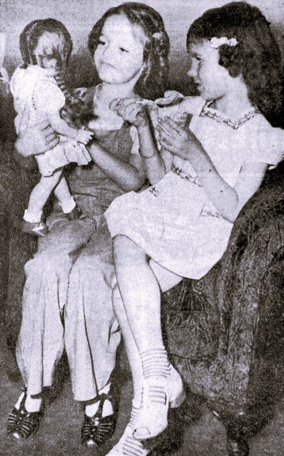 Two girls play with a doll.