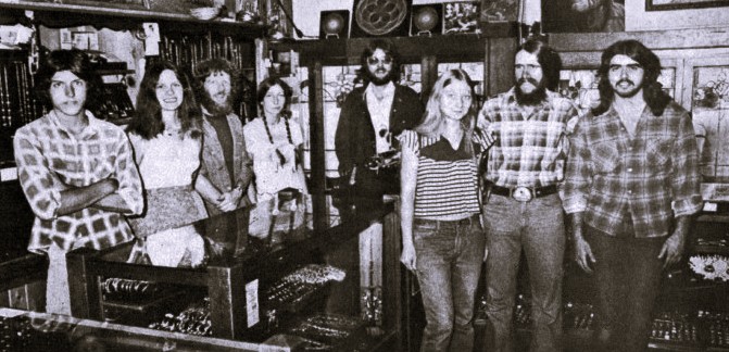 Eight young men and women pose around the display case of a store.