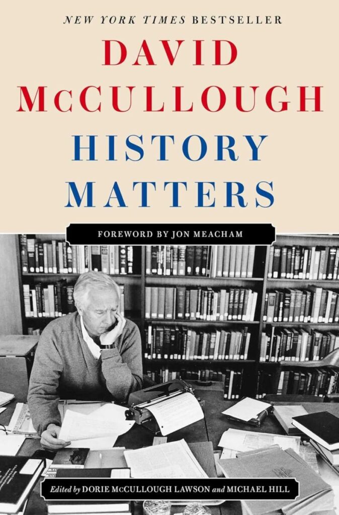 Book cover for "History Matters" by David McCullough. The top half features the title and author's name in bold red and blue text on a beige background. The bottom half features a black-and-white photograph of David McCullough sitting at a cluttered desk with a typewriter, looking thoughtfully at papers, with bookshelves filled with books in the background.