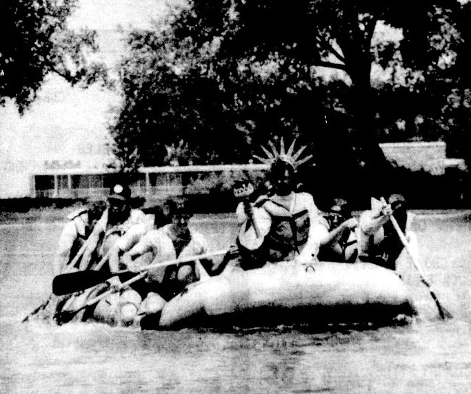 A group of rafters paddle down a river with Lady Liberty at the helm.