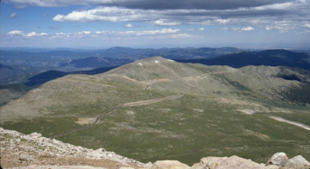 The paved byway winds through a treeless alpine tundra with mountain peaks in the background.