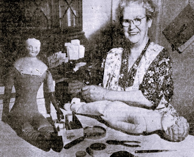 A woman repairs a doll on a workbench.