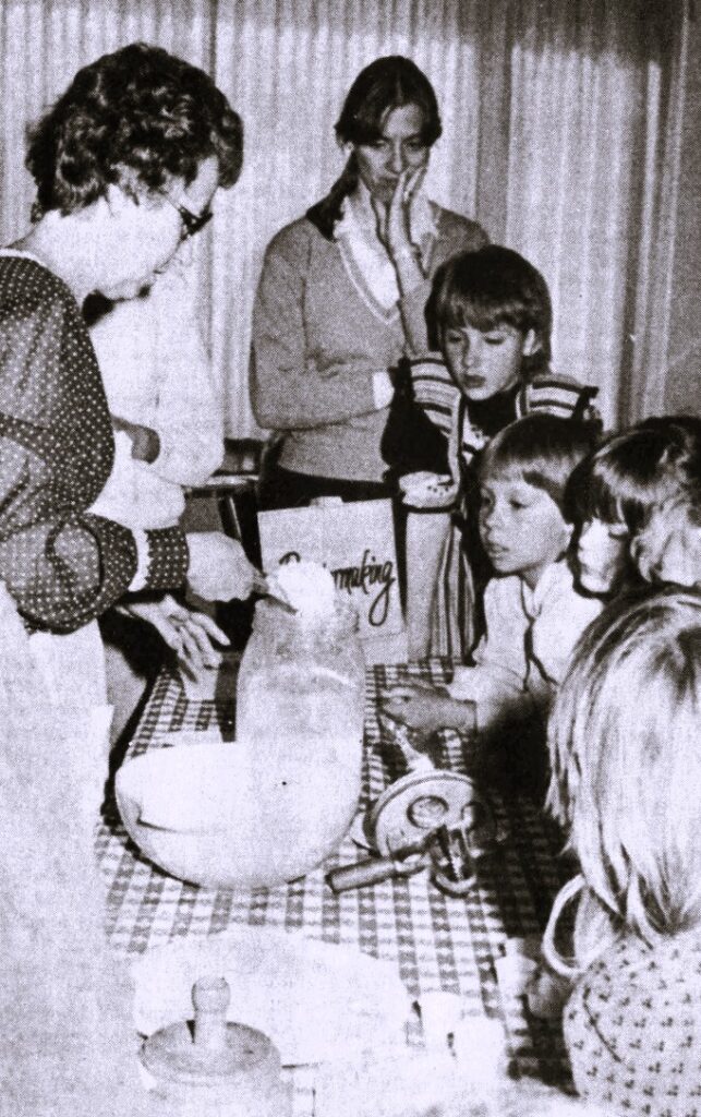 A woman demonstrates butter making to a group of children.