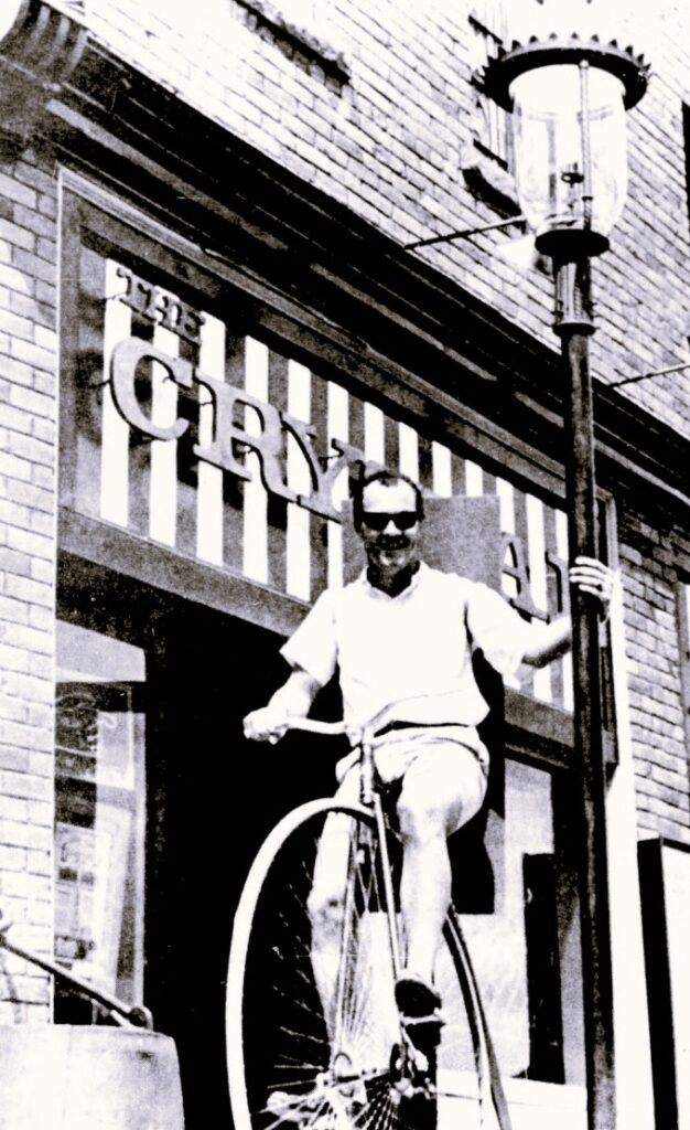 A man on a unicycle holds on to a lamp post.