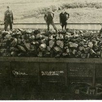 three men standing on loaded coal car