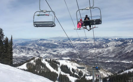 An adult and small child ride on a chairlift up a snowy mountain.