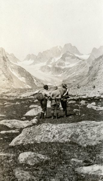 three men look at rugged mountain peaks in the distance