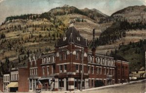 hand-colored postcard showing brick building with mountains in the background