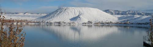 A winter landscape with a lake in the foreground and a snow-covered butte in the background