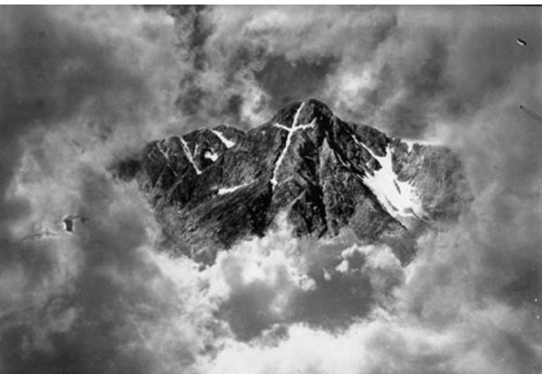 stormy clouds surround mountain with white cross of snow at its peak