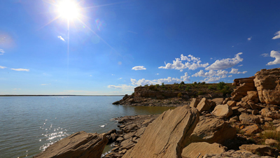 A landscape photo showing a rocky shore meeting up with a body of water under a blue sky with a few scattered clouds.