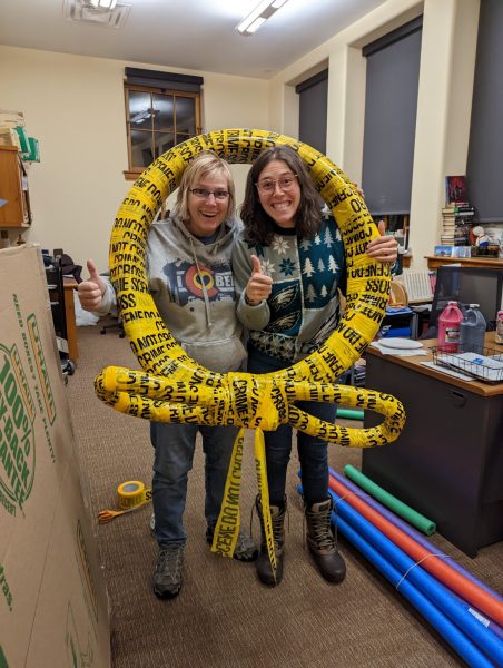 two women holding a wreath wrapped in crime scene tape smiling 