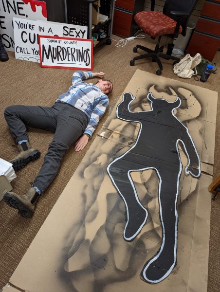 crime scene body sketch of a troll with horns cut out of cardboard and a person lying beside it in the same pose smiling 